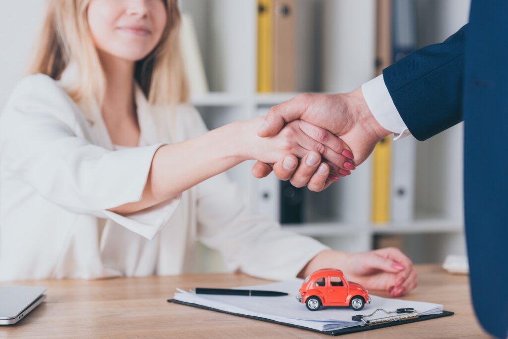 partial view of smiling woman shaking hands with car dealer in office