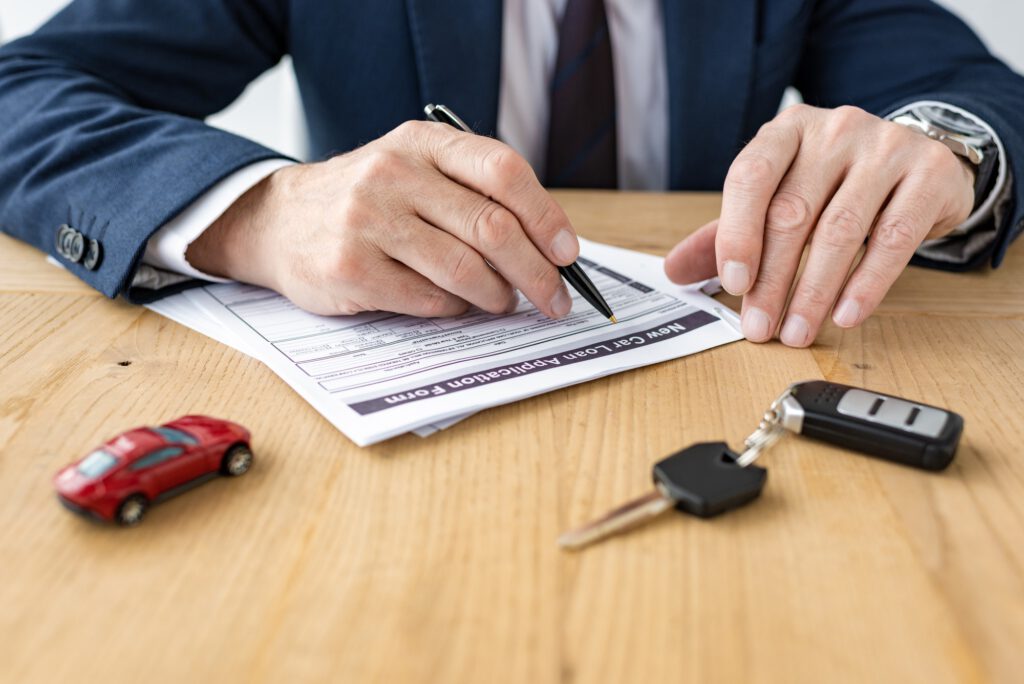 selective focus of car dealer holding pen near contract, toy car and car key